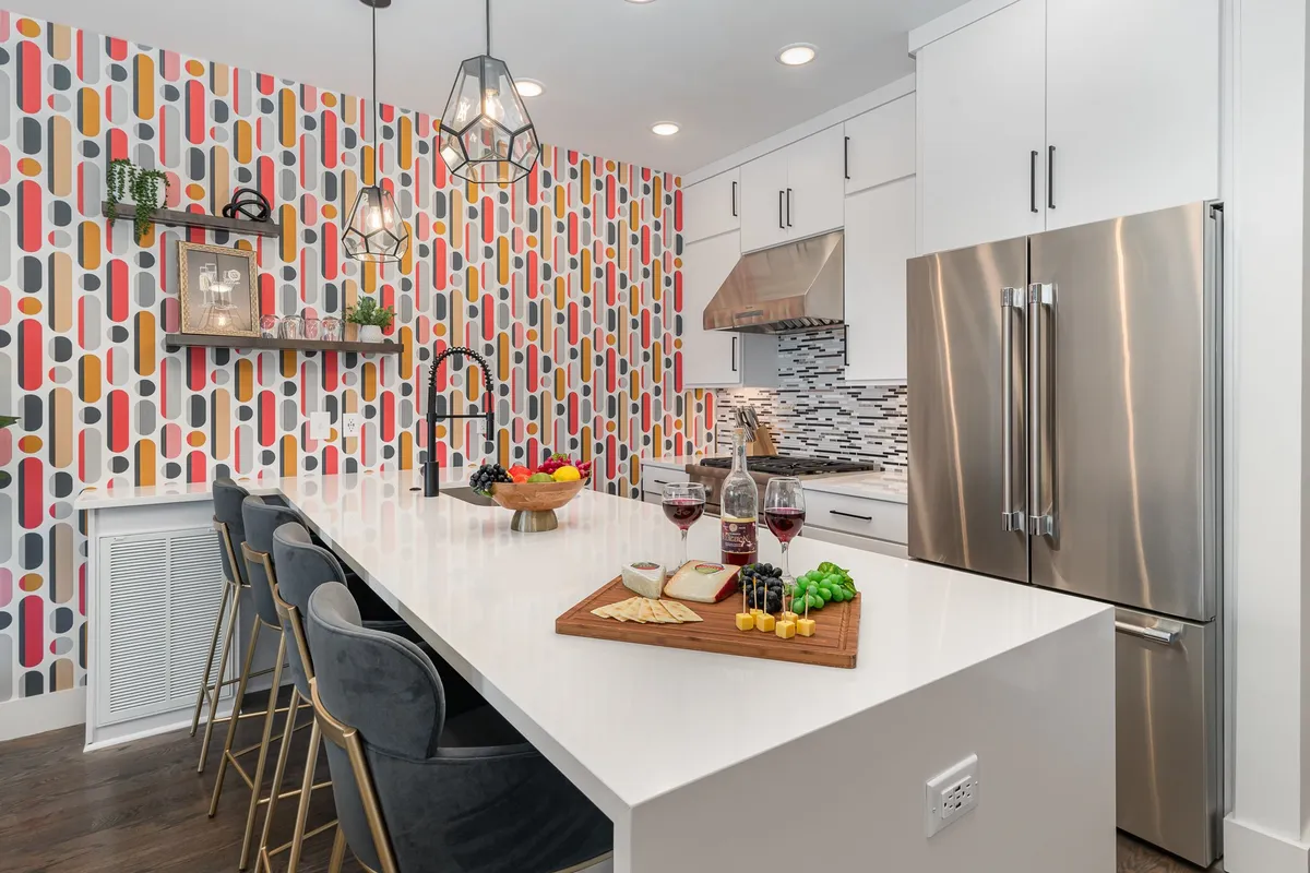 A cheerful, social kitchen scene with a colorful patterned wall, kitchen island, food platter, and wine glasses. The space is lively, evoking images of hosting dinner parties or celebrating special occasions with friends and family.