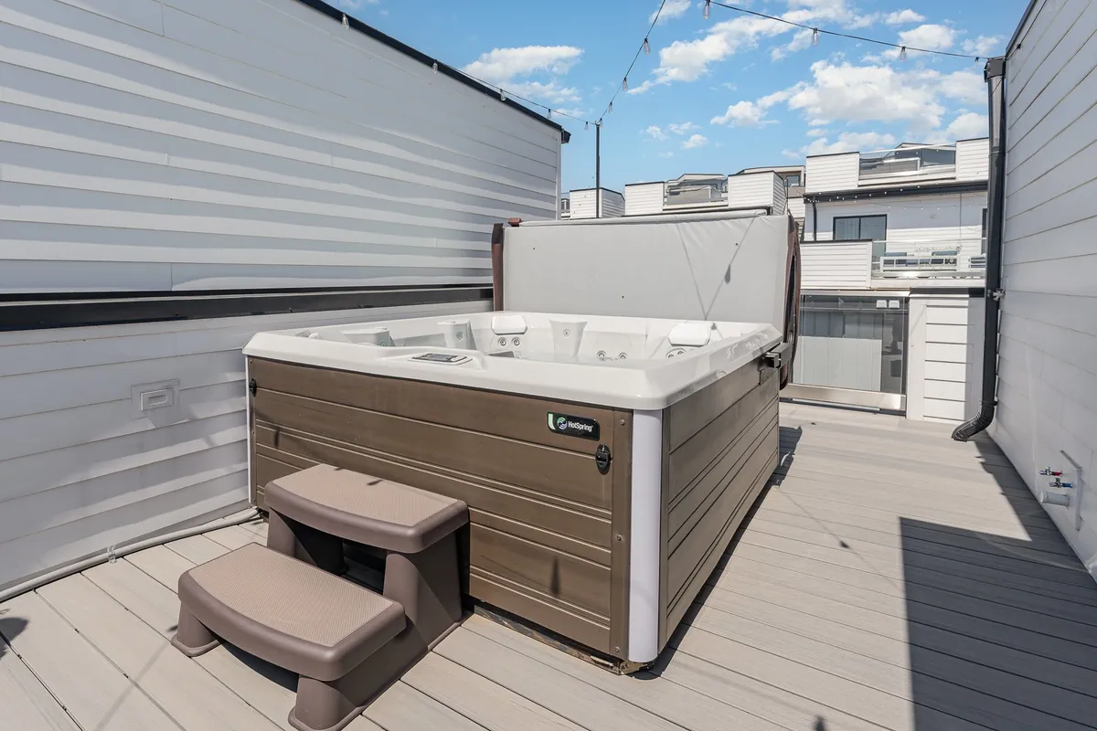 A cozy wooden rooftop deck with a hot tub as its focal point, surrounded by privacy walls. The scene is serene, inviting guests to relax in the hot tub while enjoying the open sky—ideal for both lively celebrations and quiet moments alike.