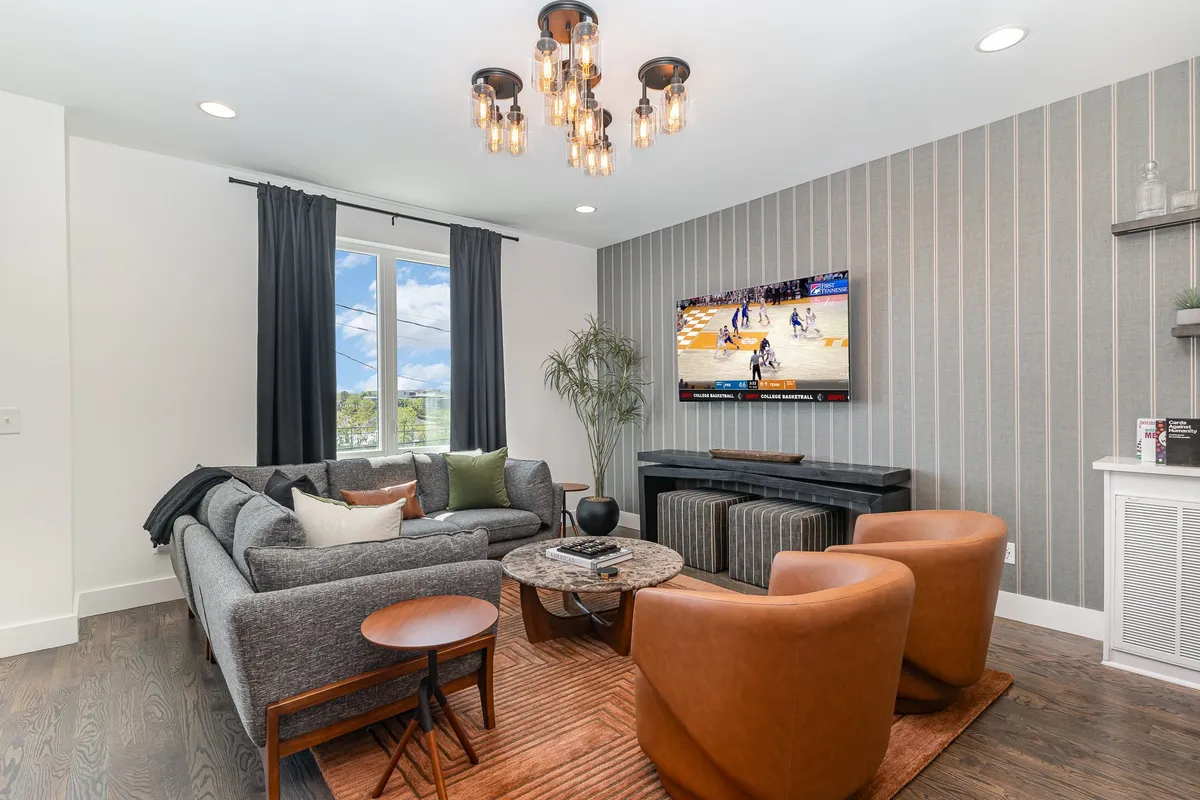 A cozy lounge area with a soft sofa, coffee table, television, elegant chandelier, and draped curtains. The setting is warm and comfortable, ideal for intimate conversations, game nights, or unwinding after a day out.