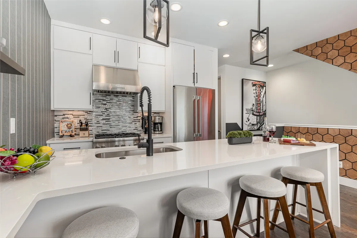 This image spotlights a kitchen with a sleek island countertop, stools, hexagonal tiled backsplash, and visible appliances. The layout is open and contemporary, ideal for interactive meal prep or casual brunches. The space feels both functional and inviting.