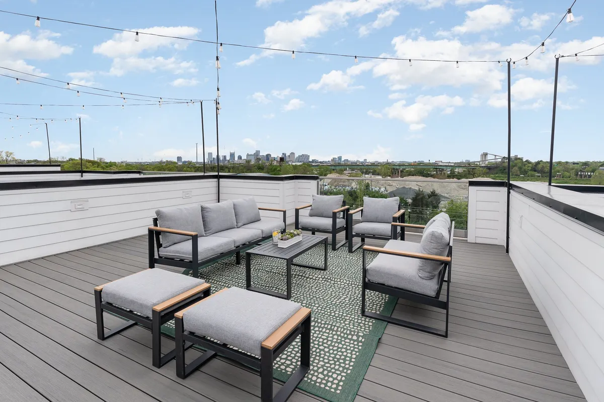An inviting rooftop lounge with comfortable outdoor seating, string lights overhead, and the Nashville city skyline in the background. The scene captures a relaxed group setting, perfect for socializing or celebrating while enjoying skyline views.