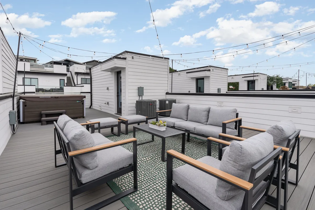 The image captures an inviting rooftop sanctuary with a bubbling hot tub, cozy outdoor seating under a canopy of glowing string lights, and panoramic skyline views—setting the stage for social gatherings, relaxing evenings, and unforgettable sunsets.