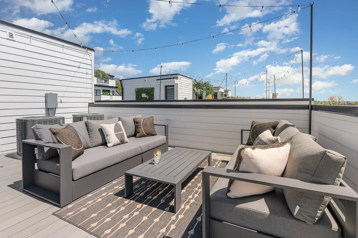 A rooftop area with a comfortable outdoor seating arrangement, decorative rug, and glowing string lights. The setting is casual and welcoming, ideal for cocktails, laughter, and gathering with friends under the evening sky.