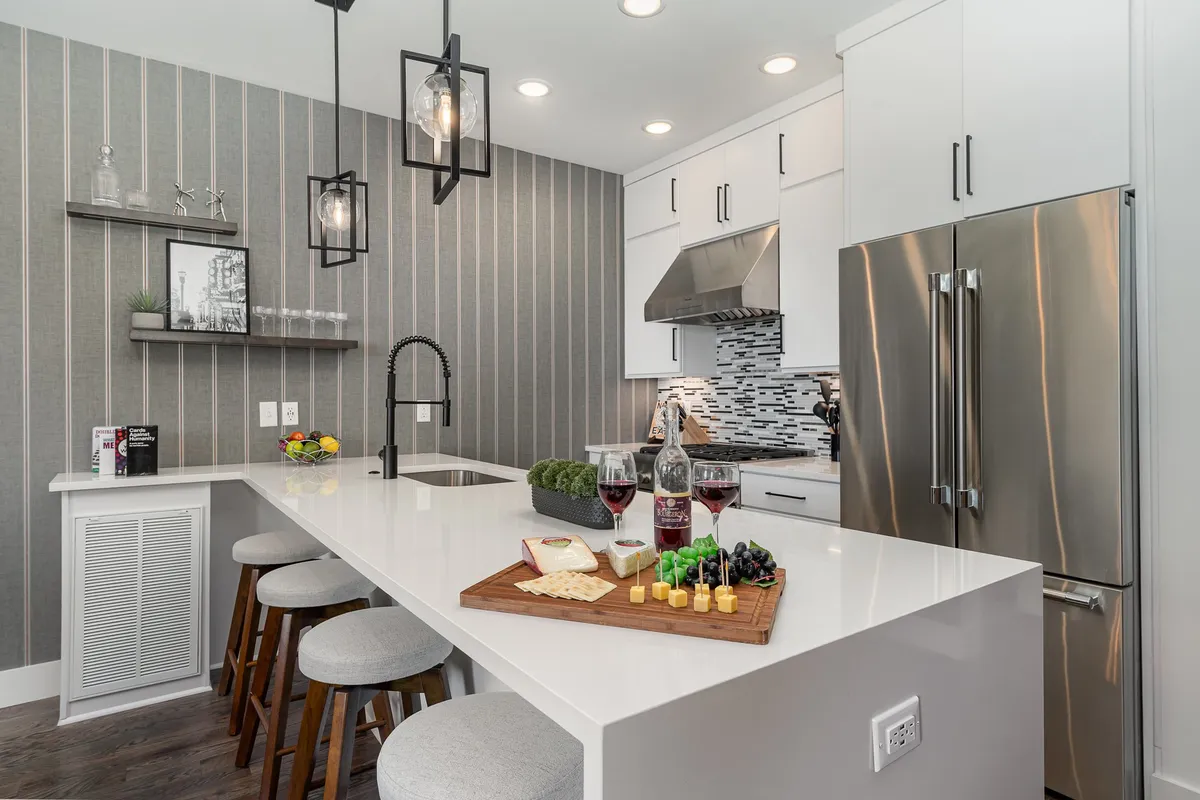 This image captures a modern kitchen island with bar stools, set under warm pendant lighting. A charcuterie board with cheese and fruits is displayed on the countertop, suggesting a space primed for both cooking and entertaining. The setting feels welcoming and cozy, inviting group gatherings or casual snacks.