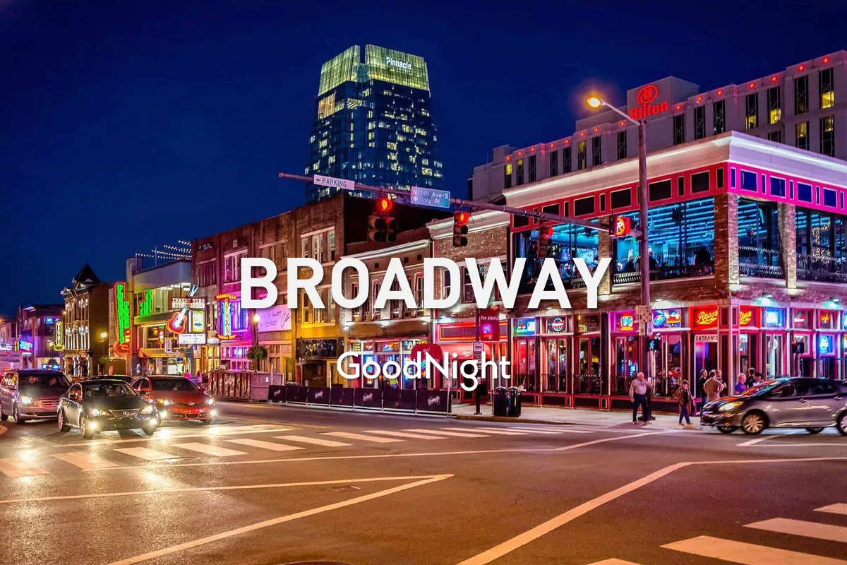 A bustling city street at night, illuminated by neon signs and energetic crowds. Cars, people, and high-rise buildings create a vibrant, urban nightlife scene, evoking the lively spirit of Broadway’s honky-tonks and music venues just minutes away.