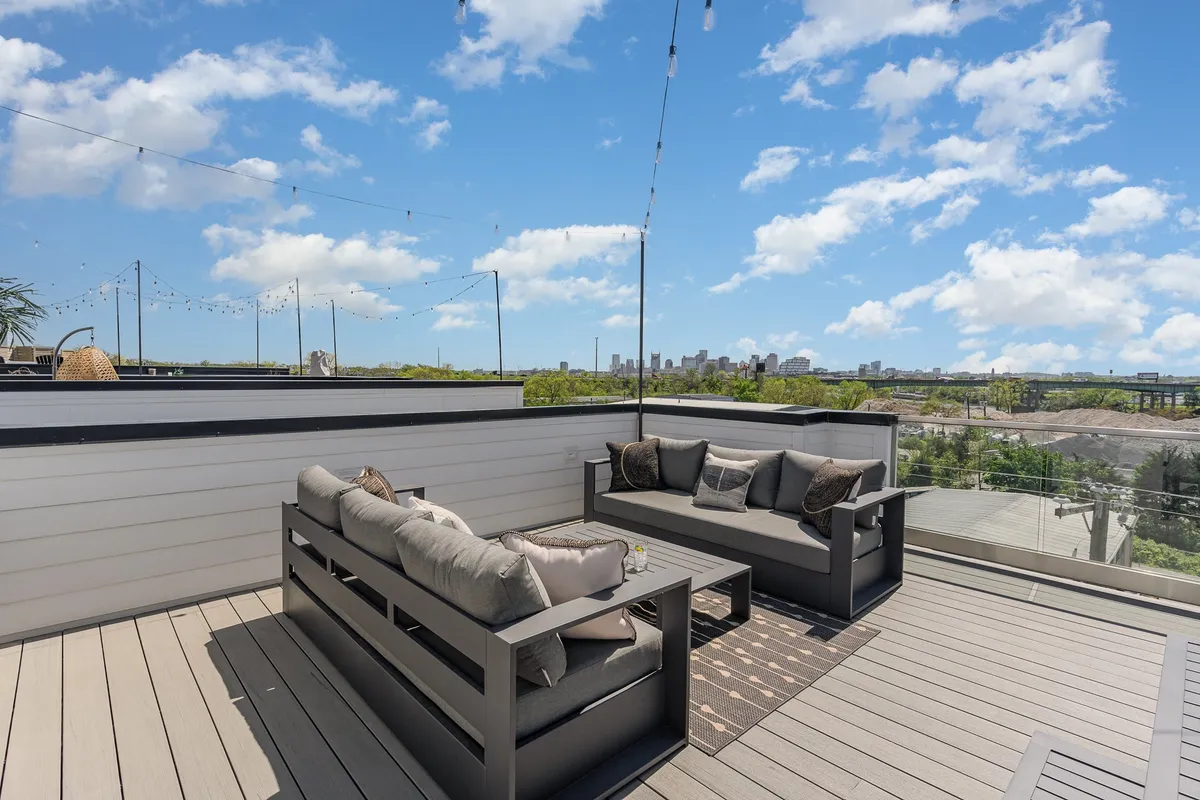 A spacious rooftop patio featuring a comfortable outdoor seating area, strings of decorative lights overhead, and a sweeping view of the city skyline at sunset. The atmosphere is tranquil yet inviting, perfect for unwinding or entertaining guests while soaking in the city energy.