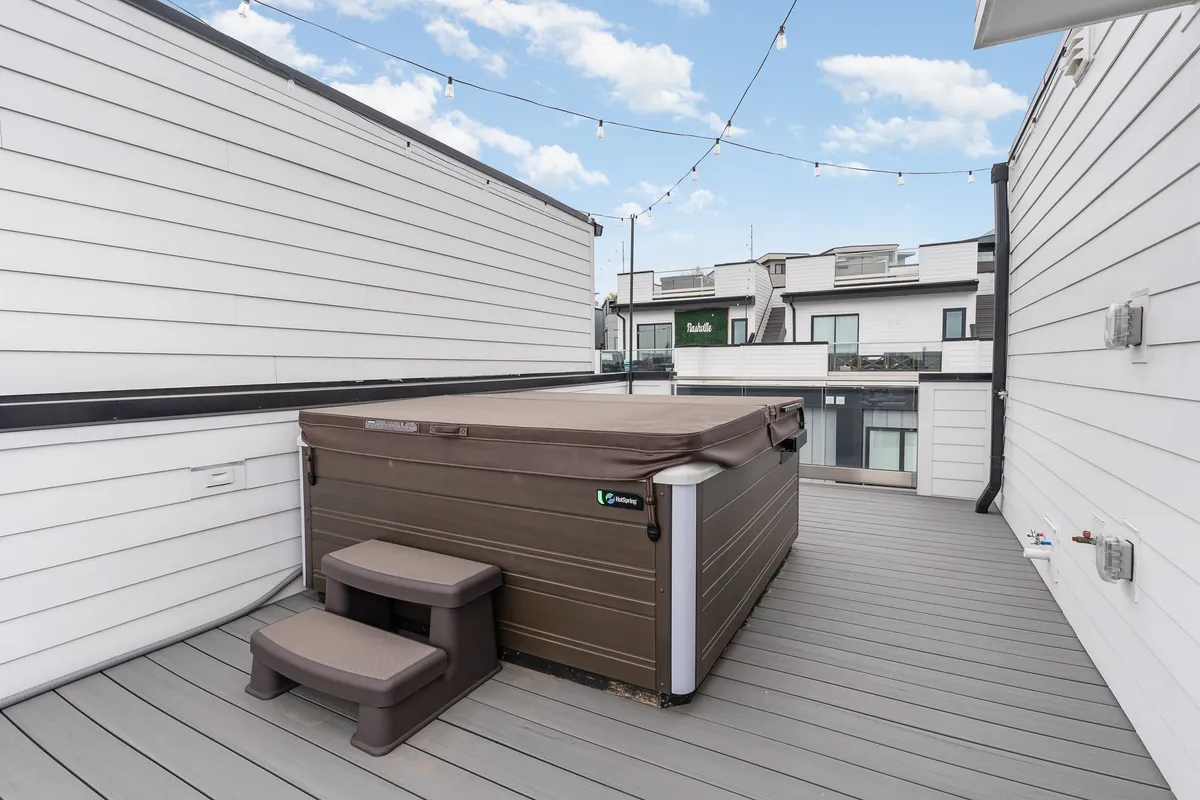 A stylish rooftop deck featuring a hot tub lit by string lights, creating a magical and relaxed evening ambiance. The space feels inviting for group gatherings, celebrations, or unwinding after a city adventure, with hints of the city skyline visible beyond the deck.